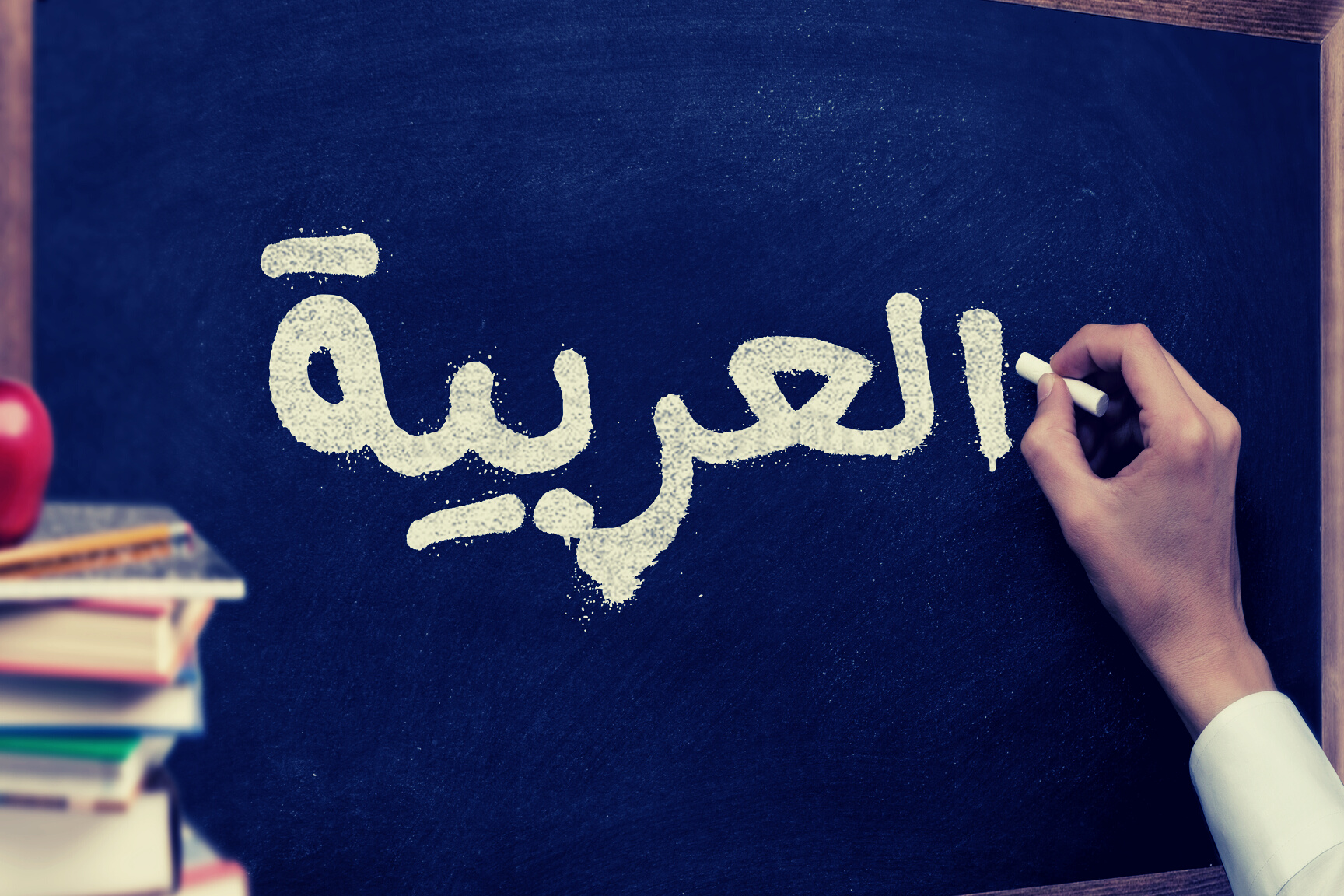 Hand writing on a blackboard in a Arabic language learning class course with the text "Arabic" written on it. with Some books and school materials concept.